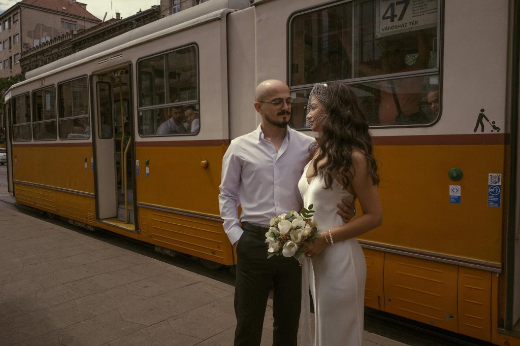 Elegant bride and groom pose by a vintage tram in Budapest, capturing timeless romance.