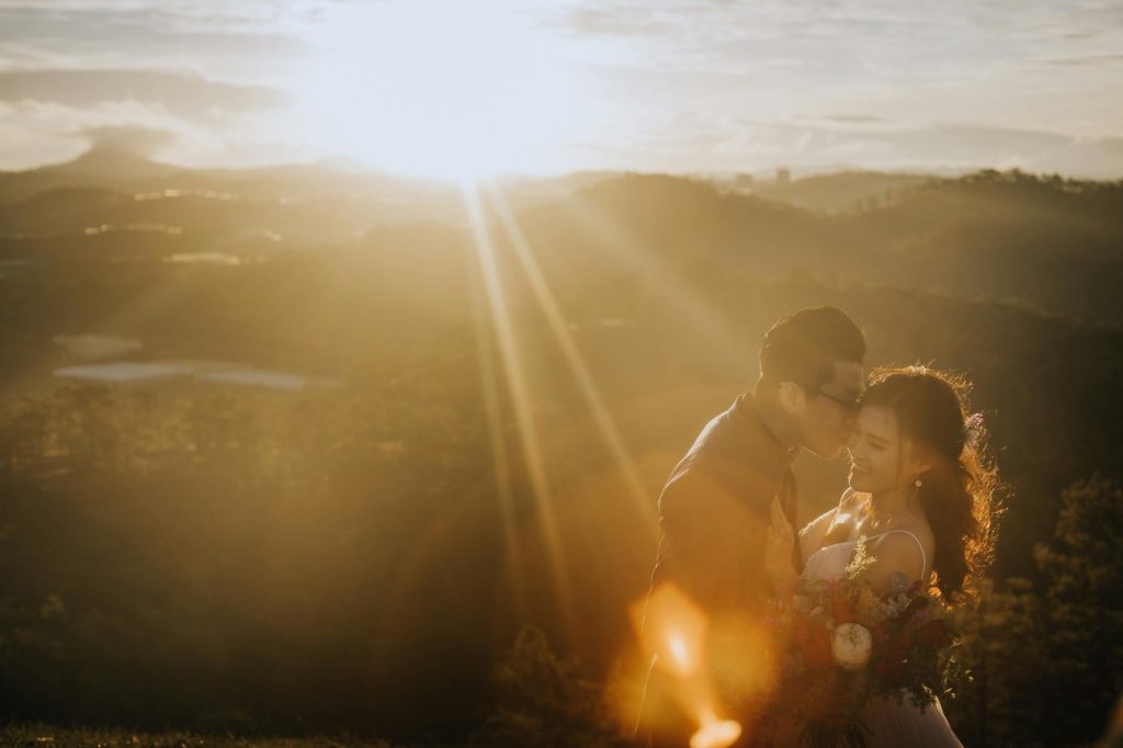 A romantic couple embracing and kissing at sunset with a scenic mountainous backdrop.