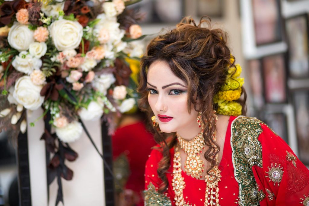 Beautiful South Asian bride in red traditional attire with floral bouquet, showcasing exquisite cultural style.