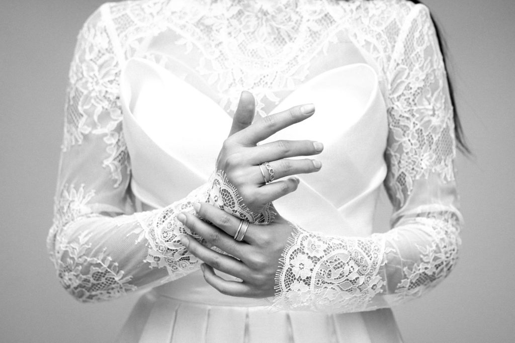 Black and white photo of a bride in a lace wedding dress, featuring elegant hands and rings.