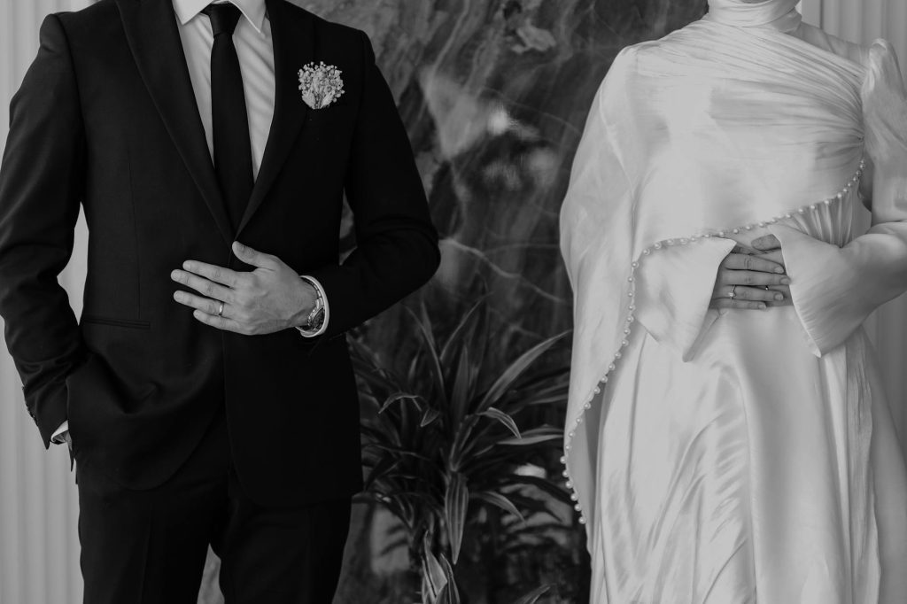 Black and white photo of a formal couple in wedding attire, emphasizing elegance.