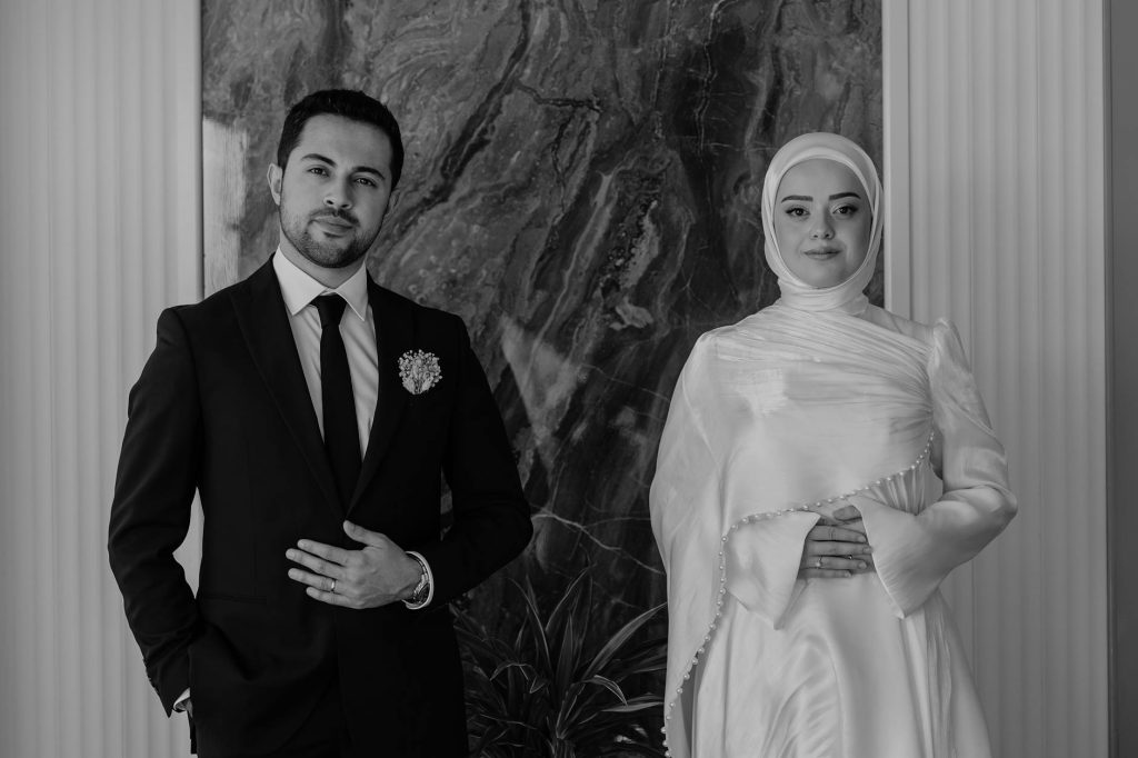 Classically styled couple in formal attire posing indoors. Black and white photo.