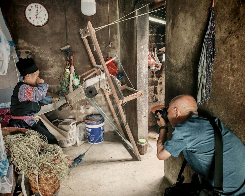 A photographer captures a traditional weaving scene inside a rustic room, showcasing cultural craftsmanship.