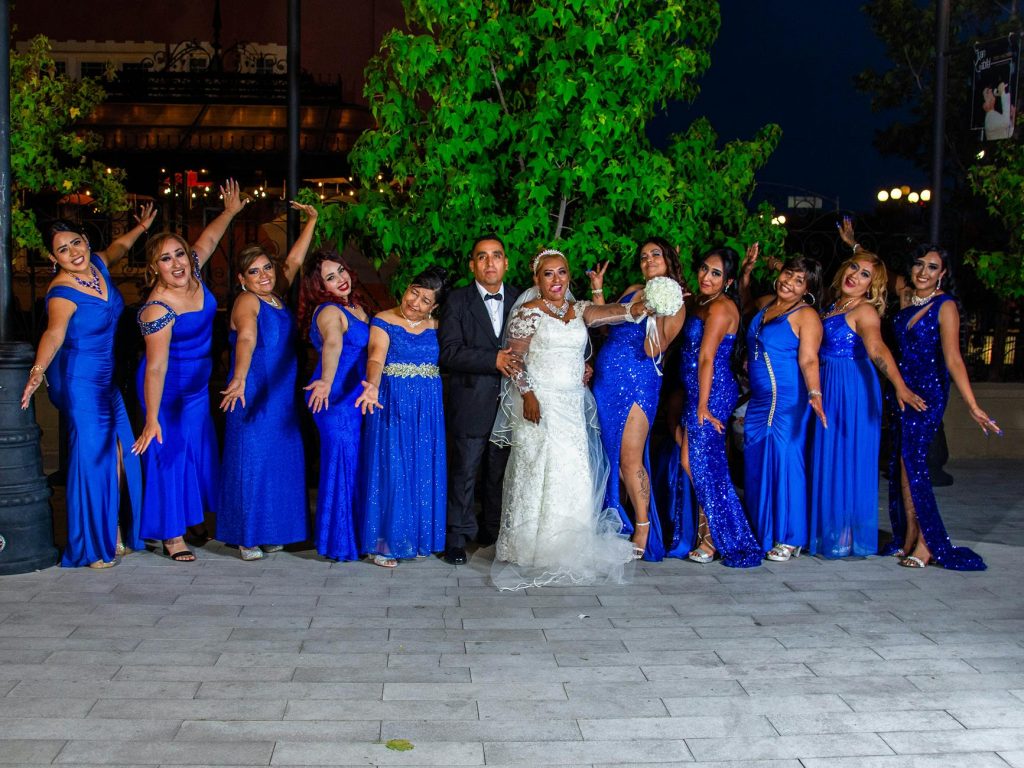 Bride and bridesmaids in blue dresses pose outdoors at night, capturing joyful wedding moments.