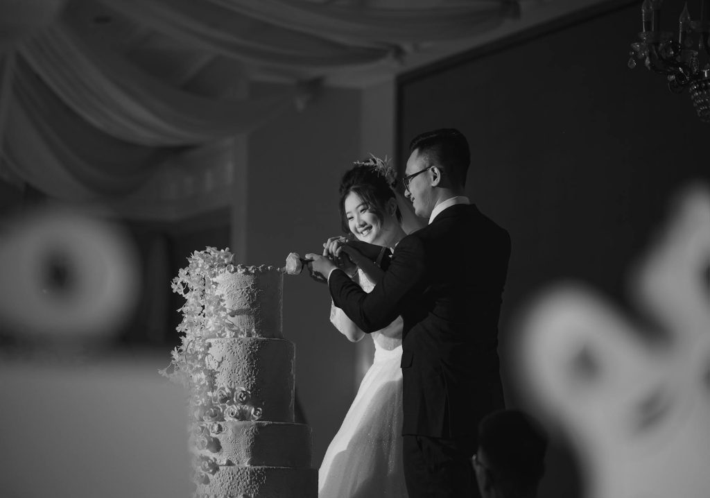 A couple joyfully cuts their wedding cake in a classic black and white setting, capturing timeless elegance.