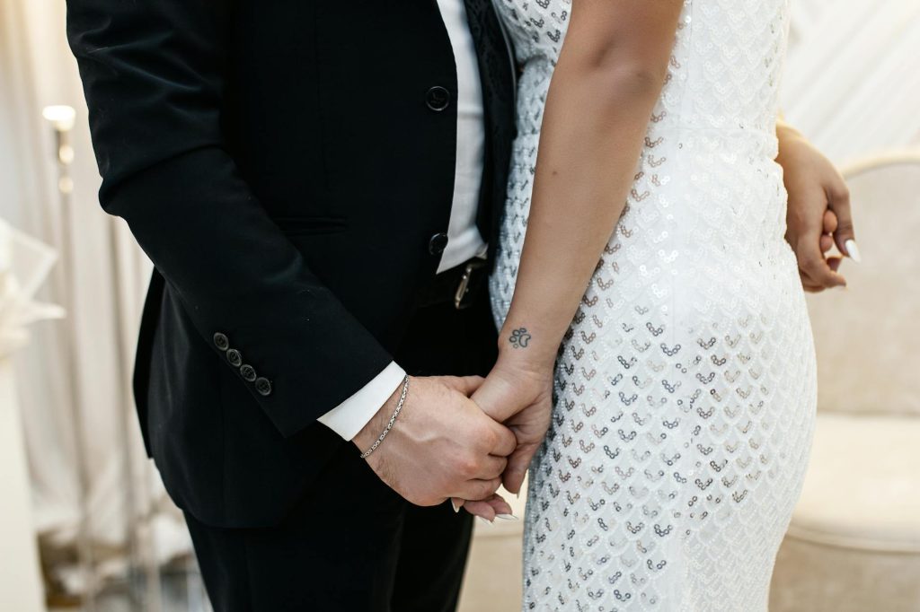 A close-up of a couple holding hands, showcasing elegant wedding attire.