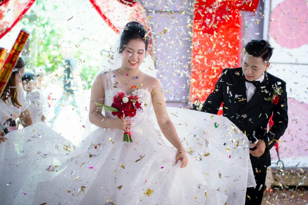 Vibrant wedding scene in Vietnam with bride and groom celebrating amidst colorful confetti shower.