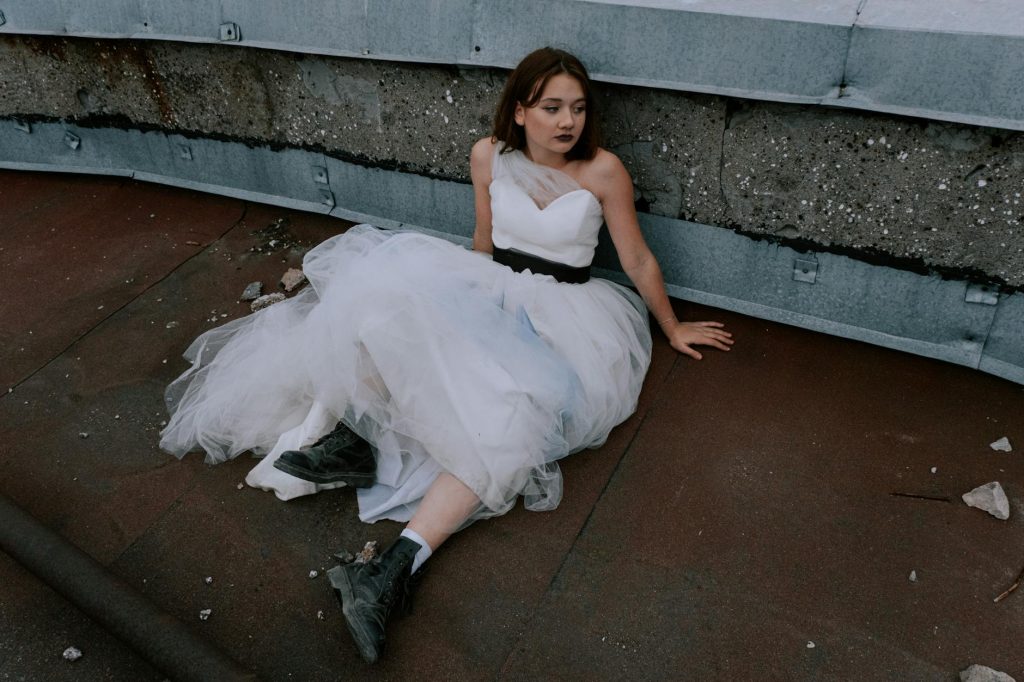 Bride in a wedding gown seated on urban rooftop, blending elegance with grit.