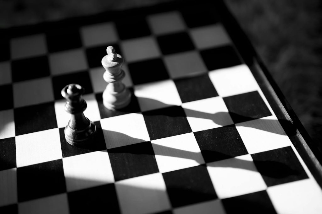 Black and white chess pieces casting long shadows on a chess board, creating a dramatic and strategic mood.