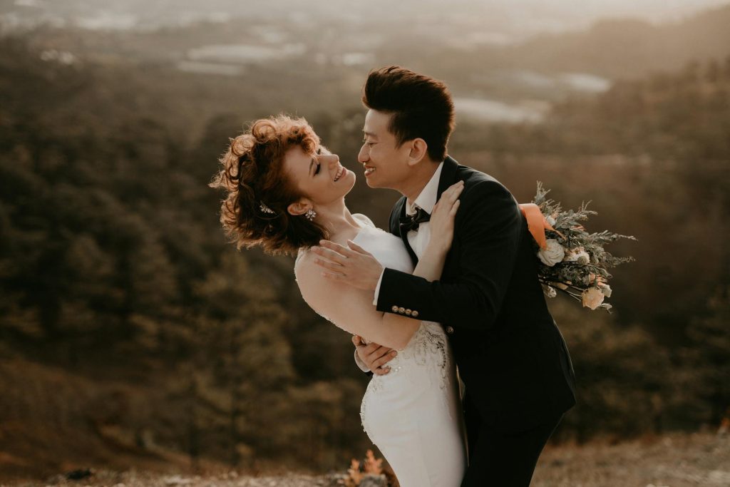 Bride and groom share a joyful embrace outdoors during a warm sunset, capturing a romantic wedding moment.