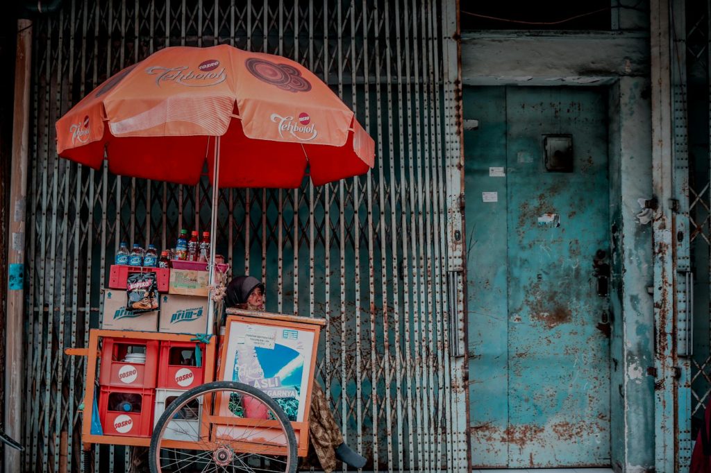 A street vendor selling drinks in Indonesia under a colorful umbrella.