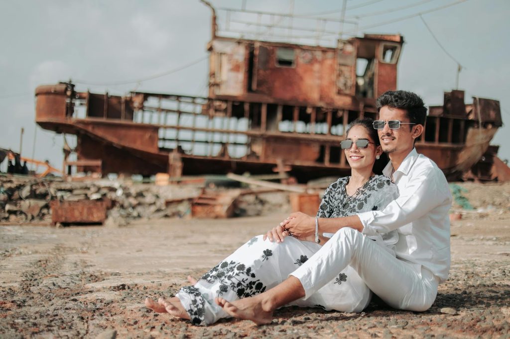 A happy couple poses by an old shipwreck in Mandvi, Gujarat, India, exuding warmth and love.