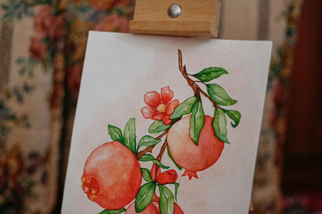 A vibrant watercolor painting of pomegranates and flowers on an easel, showcasing artistic talent.