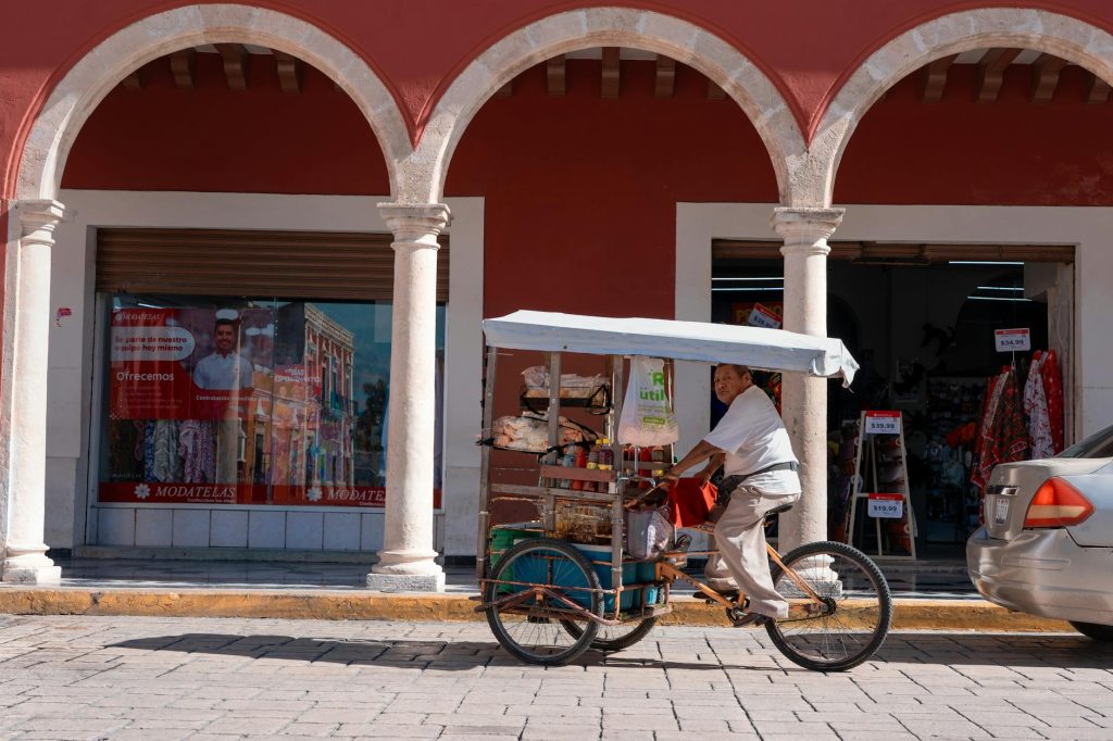 A street vendor on a tricycle sells goods outside historic arches in San Francisco de Campeche.