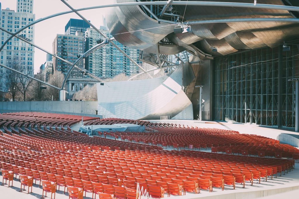 Futuristic outdoor amphitheater featuring red seats and glass panels in an urban setting.