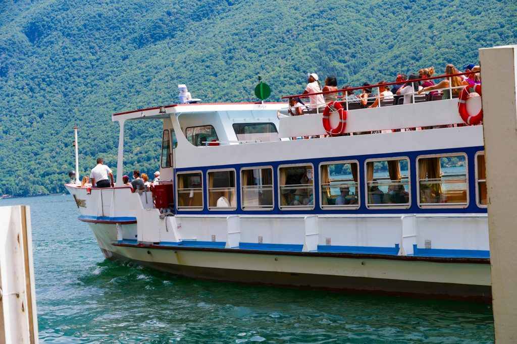 A scenic cruise boat filled with tourists, set against lush Swiss mountains on Lake Lugano.