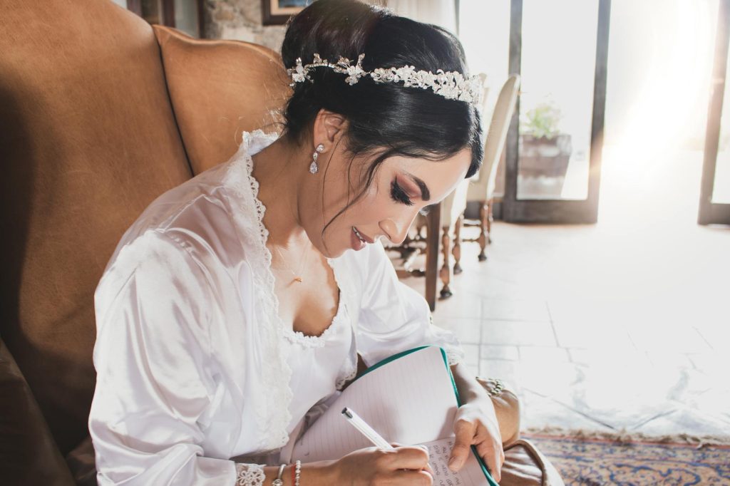 Bride in wedding robe writing notes in a notebook during her wedding morning preparation.