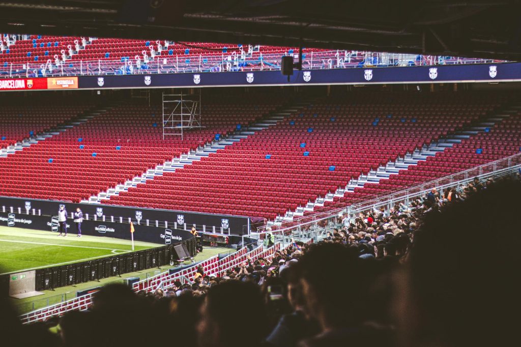 Panoramic view of stadium with empty red seats and crowd gathered for a live match.