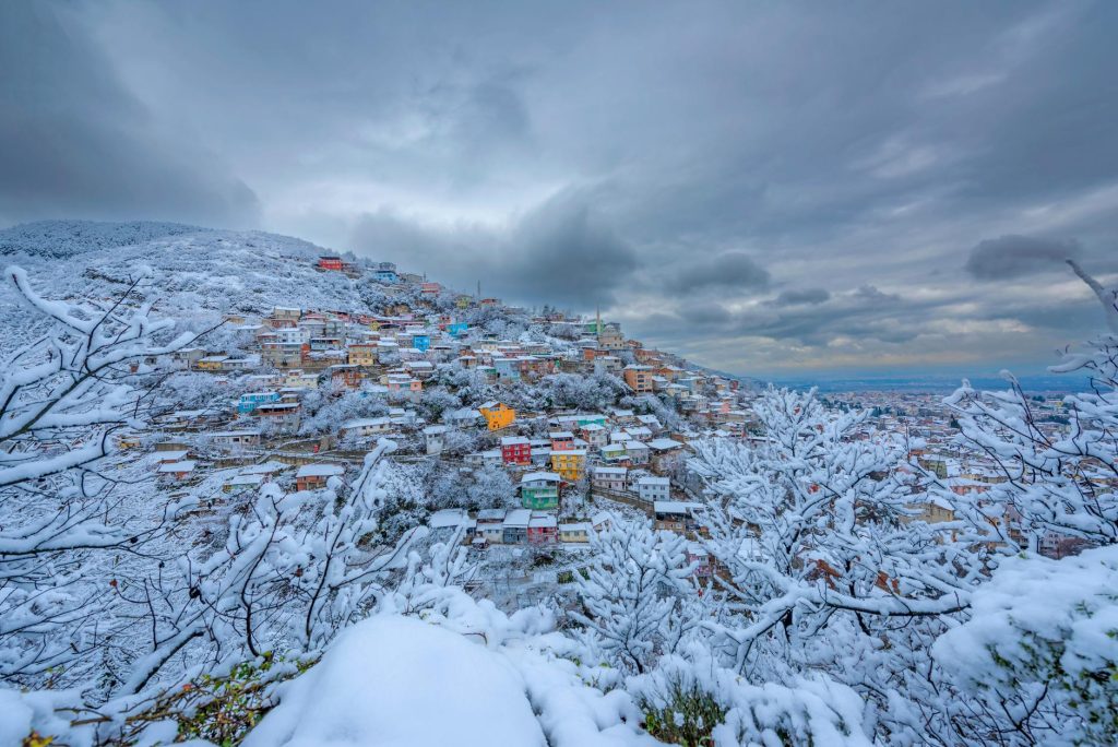 Colorful houses in snow-covered Bursa, Türkiye, under a cloudy winter sky.