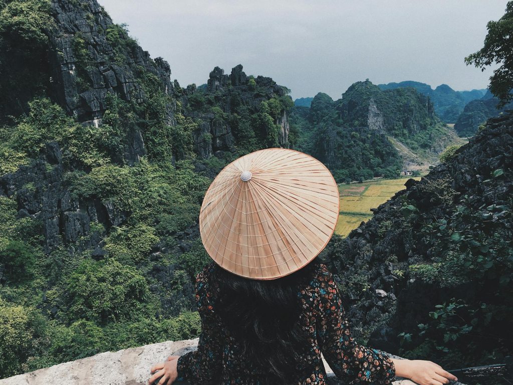 Woman in traditional hat overlooks stunning limestone cliffs in Ninh Binh, Vietnam.