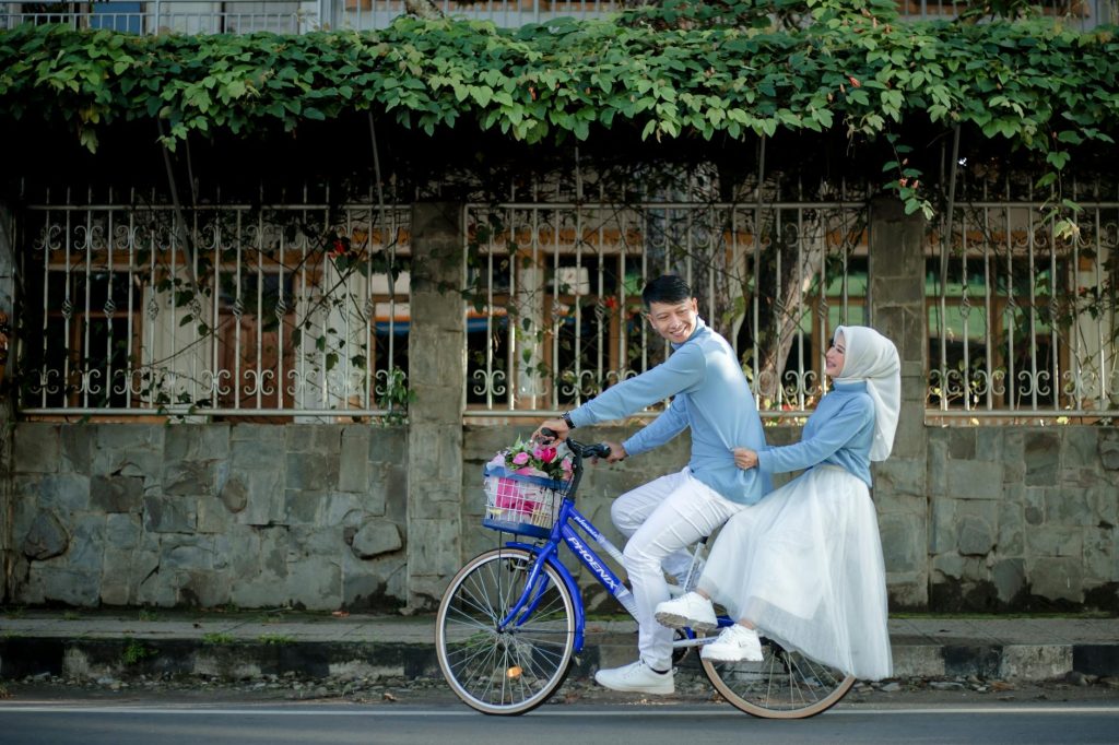 A joyful couple enjoying a playful moment on a bicycle for their prewedding photo shoot outdoors in Indonesia.