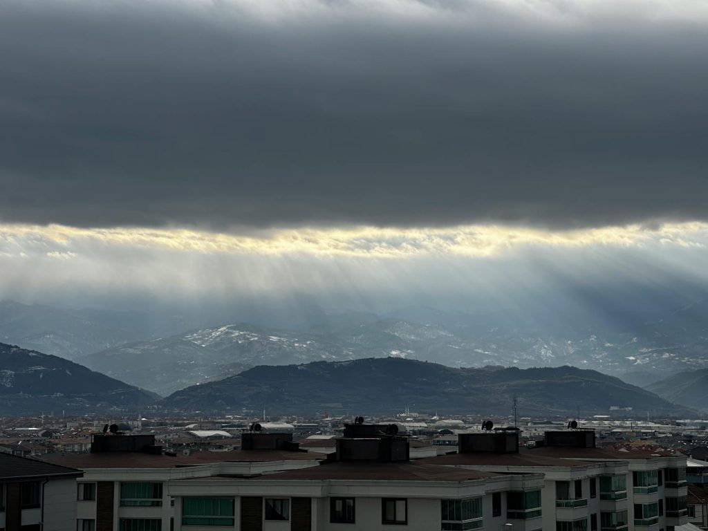A breathtaking view of sunlight breaking through dark clouds over a city with distant mountains.