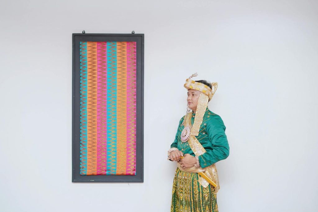 Makassar groom in colorful traditional attire with vibrant textile art.