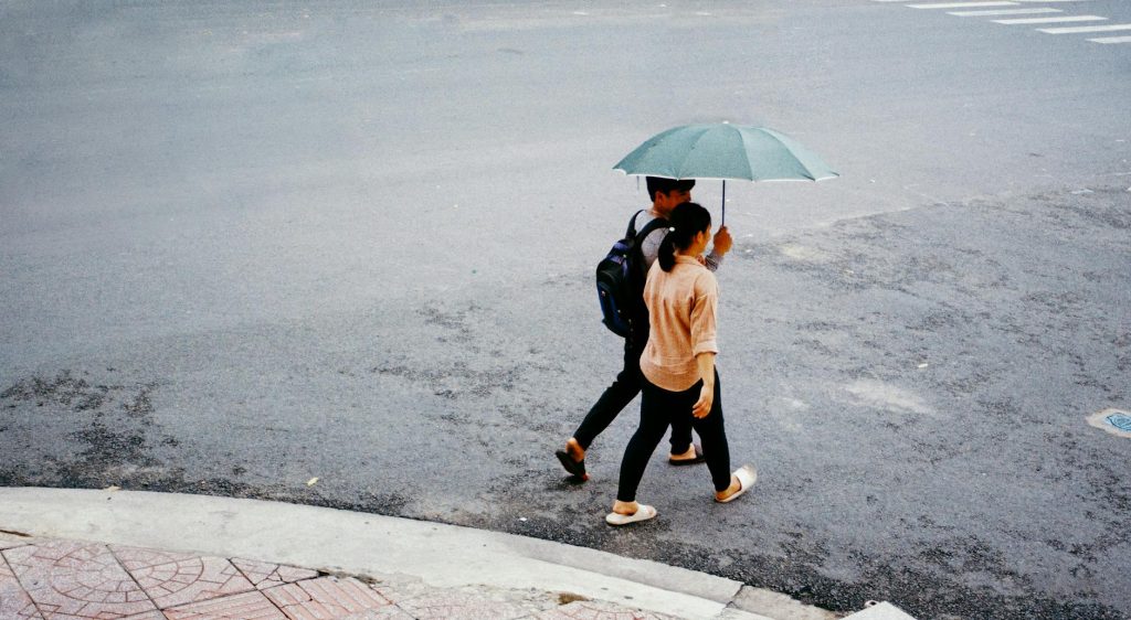 A couple walks under a green umbrella across a street, offering a candid city scene.
