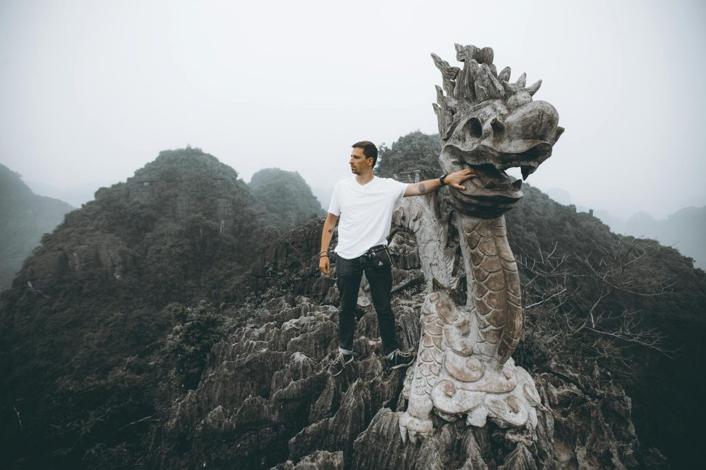 Man poses with a dragon sculpture atop Mua Cave, amidst the stunning limestone peaks of Ninh Bình, Vietnam.