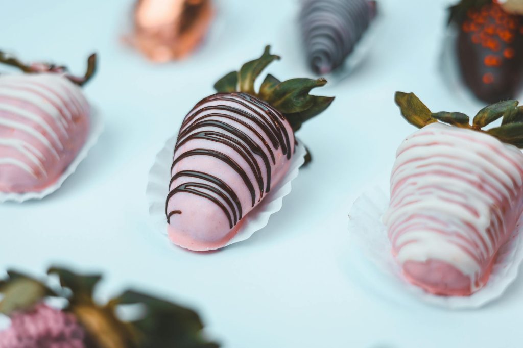 A close-up of assorted pink and chocolate-dipped strawberries showcasing intricate designs, perfect for weddings and celebrations.