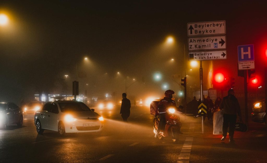 A moody nighttime street scene in Istanbul featuring vehicles, road signs, and city life.