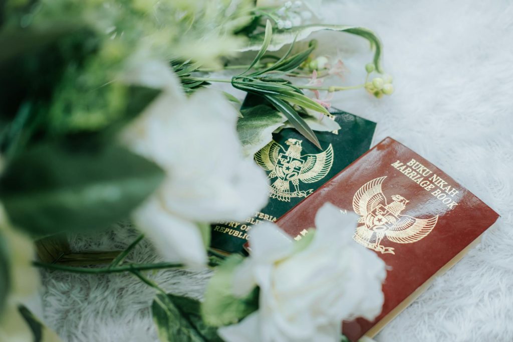 Close-up of Indonesian marriage books surrounded by a floral arrangement on a soft surface.