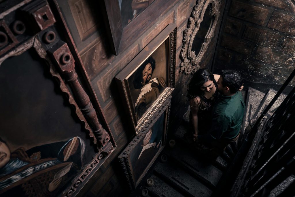 Asian couple in a vintage setting, surrounded by classic art, sharing an intimate moment on a staircase.