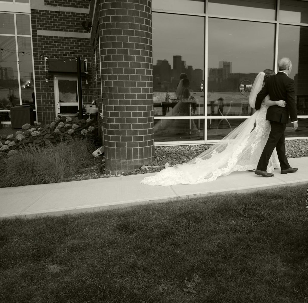 Bride and groom walking outside venue with Boston skyline reflection.