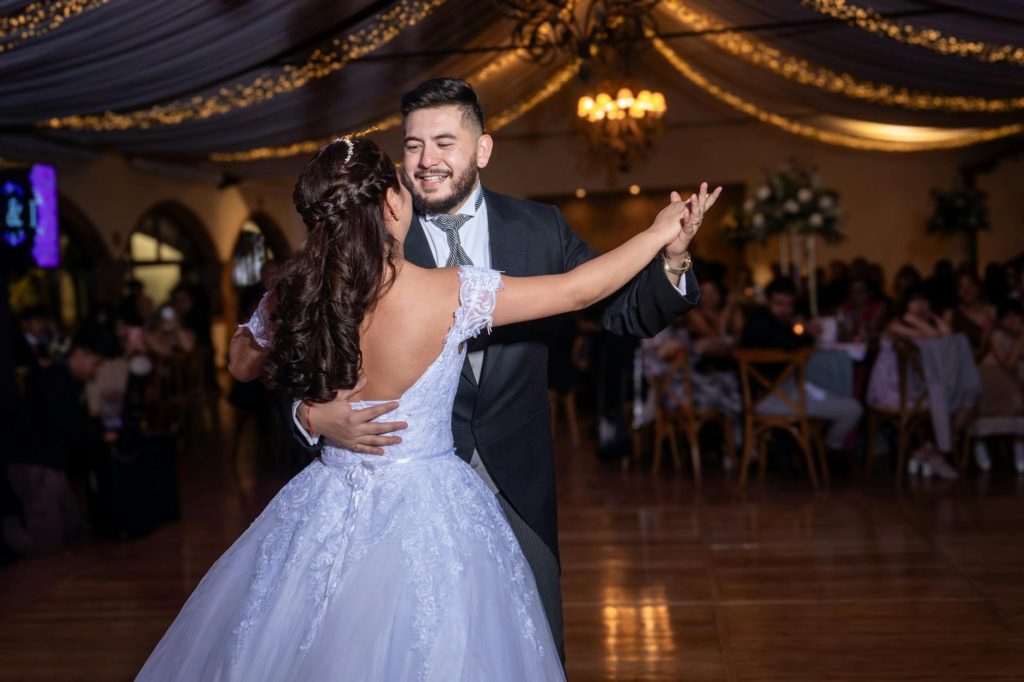 A couple sharing a joyful dance at a wedding in México's elegant ballroom lighting.