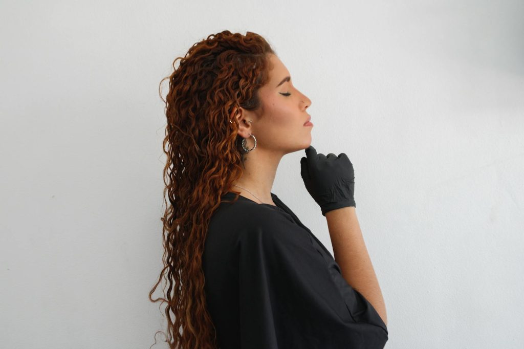 Profile of a redhead woman in thoughtful pose, wearing black attire and gloves.