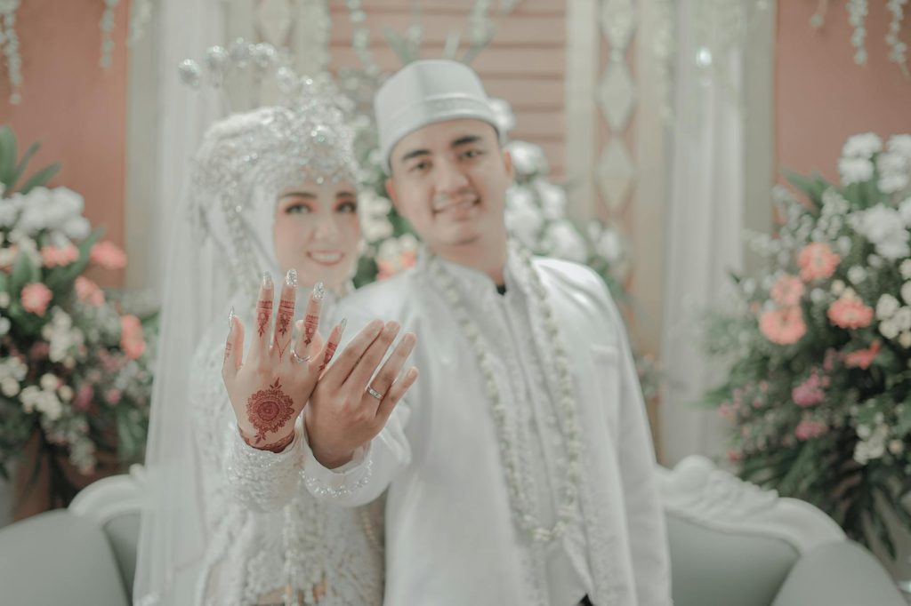 A happy couple in elegant attire showcasing their wedding rings and intricate henna design.