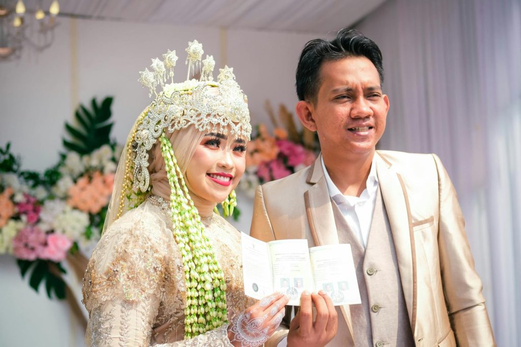 Smiling Indonesian Muslim couple in traditional attire during their joyful wedding celebration.