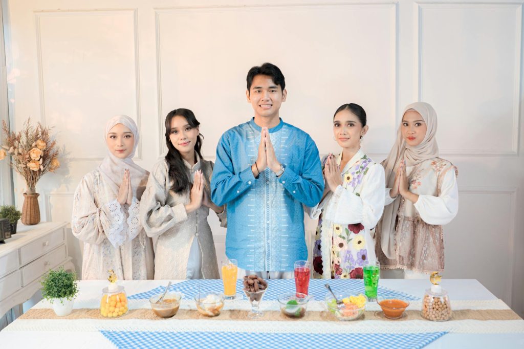 Five adults in traditional attire gather indoors with food and drinks, demonstrating cultural celebration in Jakarta.