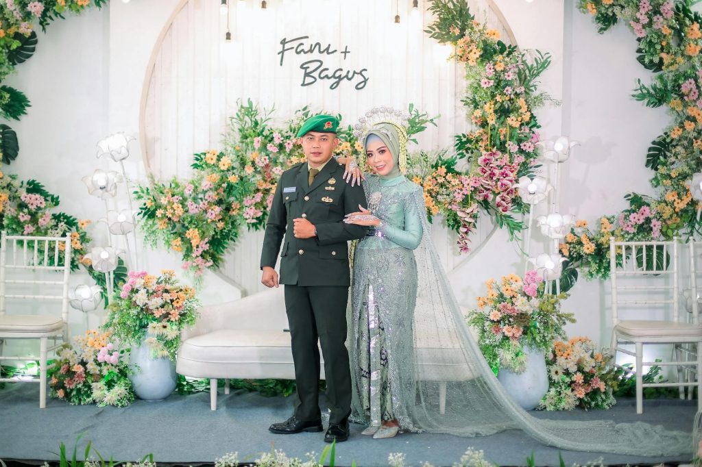 Stunning wedding photo featuring bride in silver gown and groom in military uniform amidst floral decor.