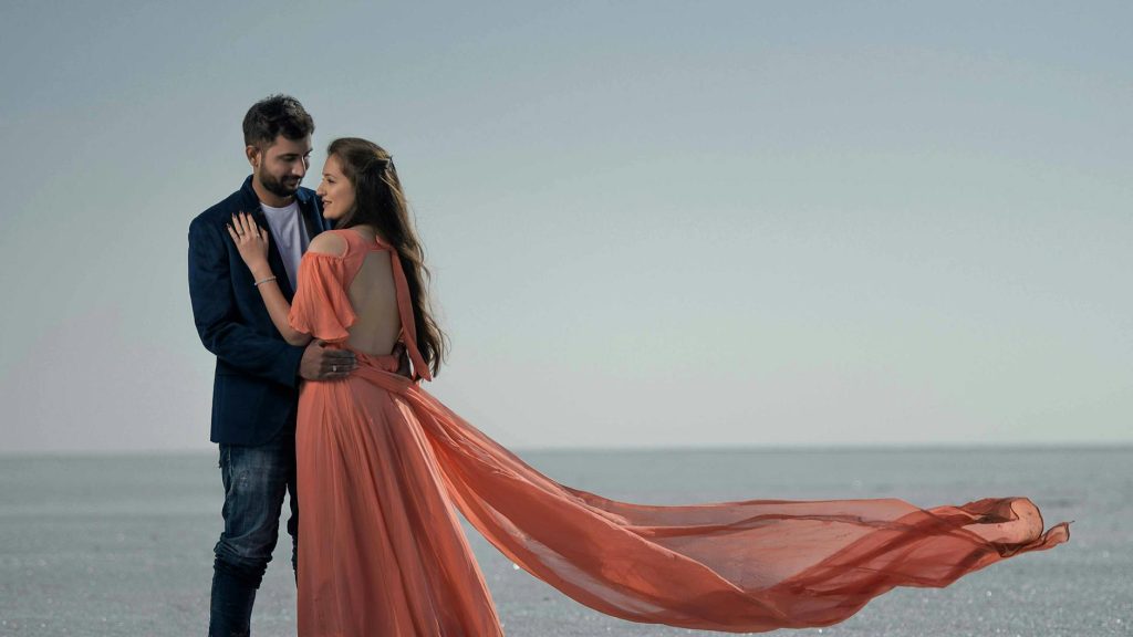 A couple embracing by the ocean with flowing dress, captured in a serene outdoor setting.