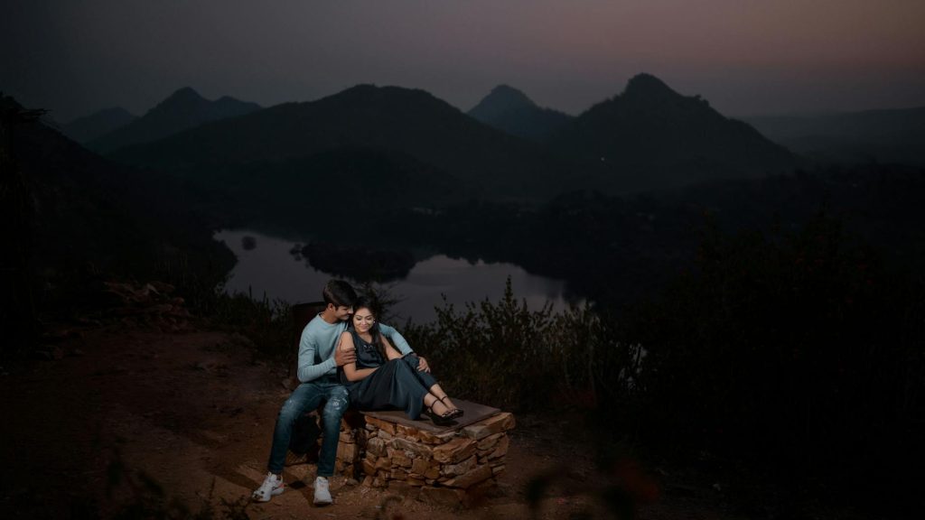 A couple shares a tender moment at twilight in a picturesque mountain landscape.